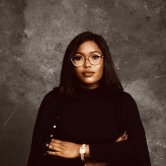 Christiana Kayode smiling at the camera against a gray background.